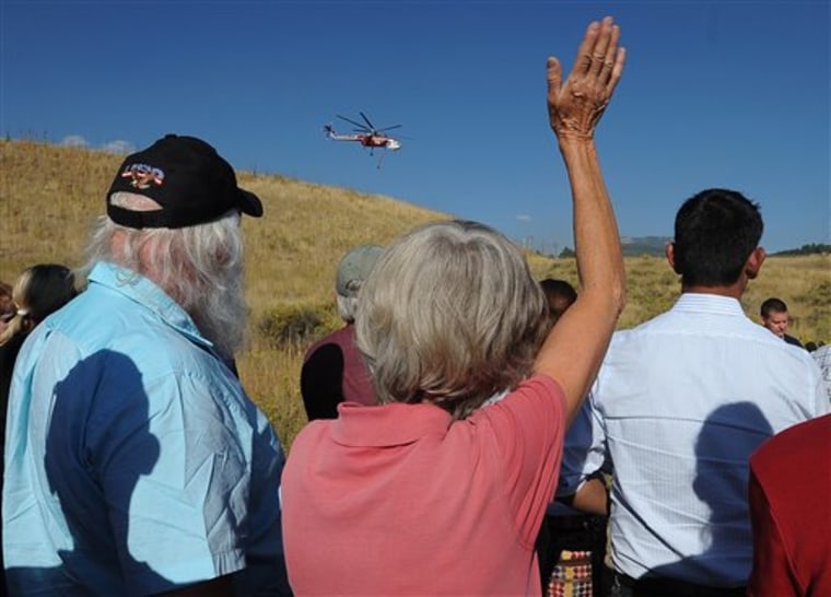 Fire victim Helen Grissom waves to a helicopter as it passes above on Tuesday. The helicopter was flying from Flatiron Reservoir after siphoning a tank full of water to drop on the fire west of Loveland, Colo. 